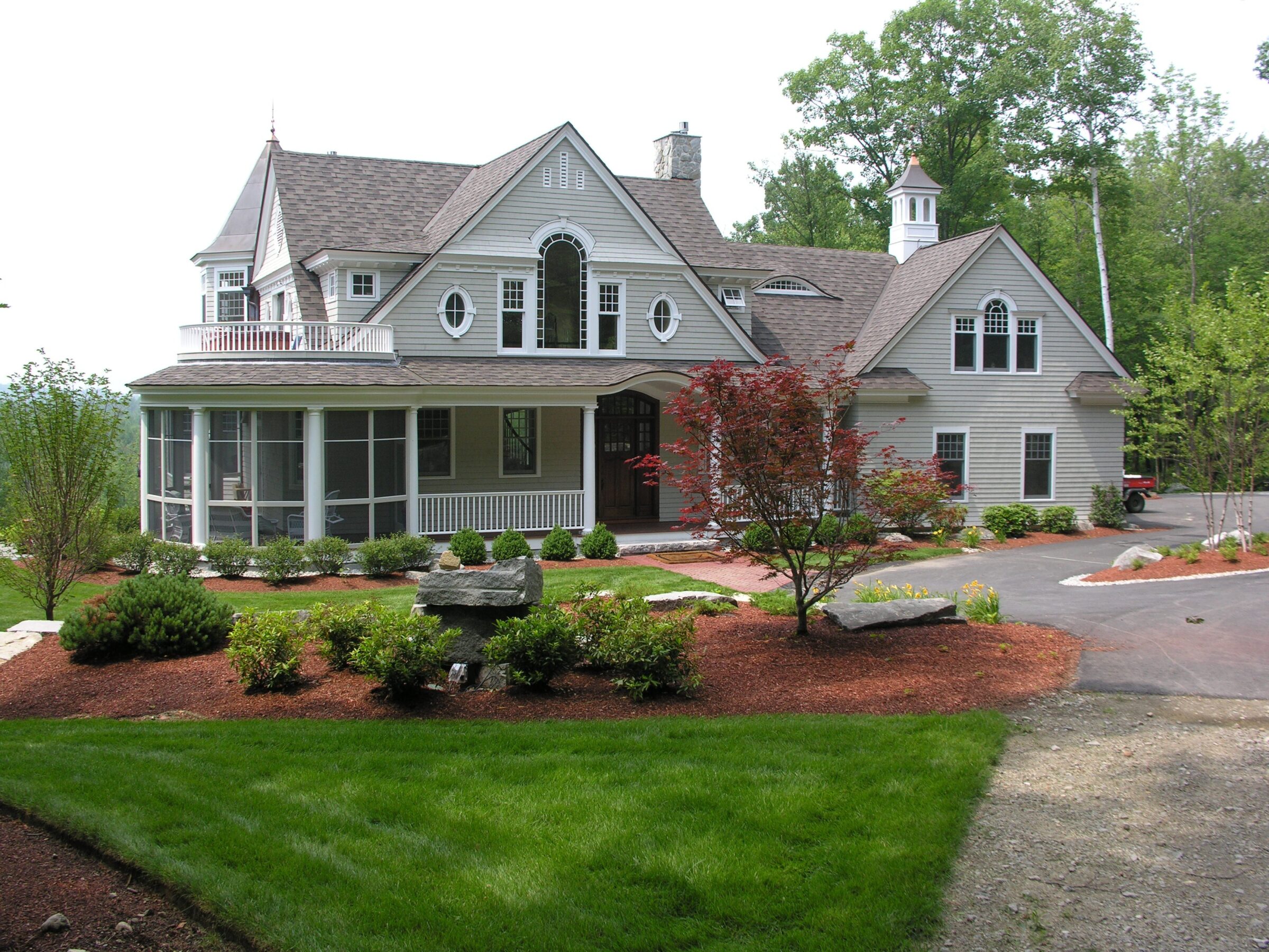 A charming Victorian-style house with gabled roofs, surrounded by manicured gardens and lush greenery, under a clear sky.