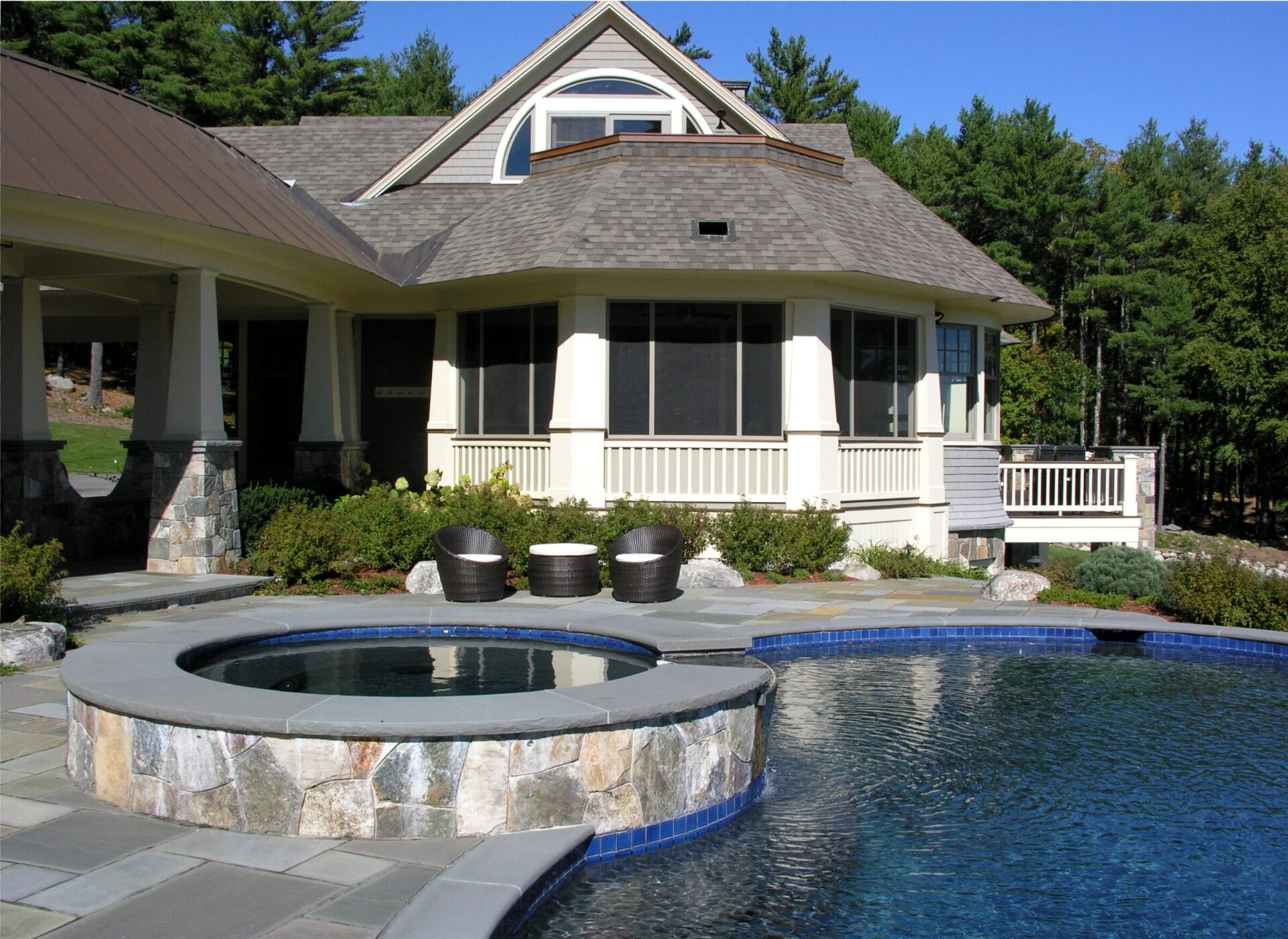 A modern house with a large pool and hot tub set amid lush greenery, featuring stone and wood architecture and outdoor seating.