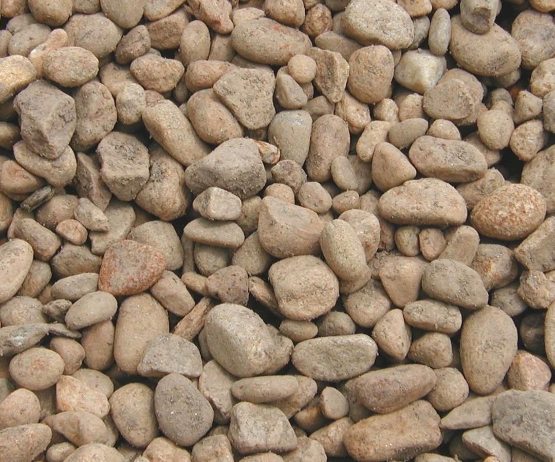 A close-up image of numerous small, round, natural stones in varying shades of brown, creating a textured, earthy pattern. No people or landmarks.