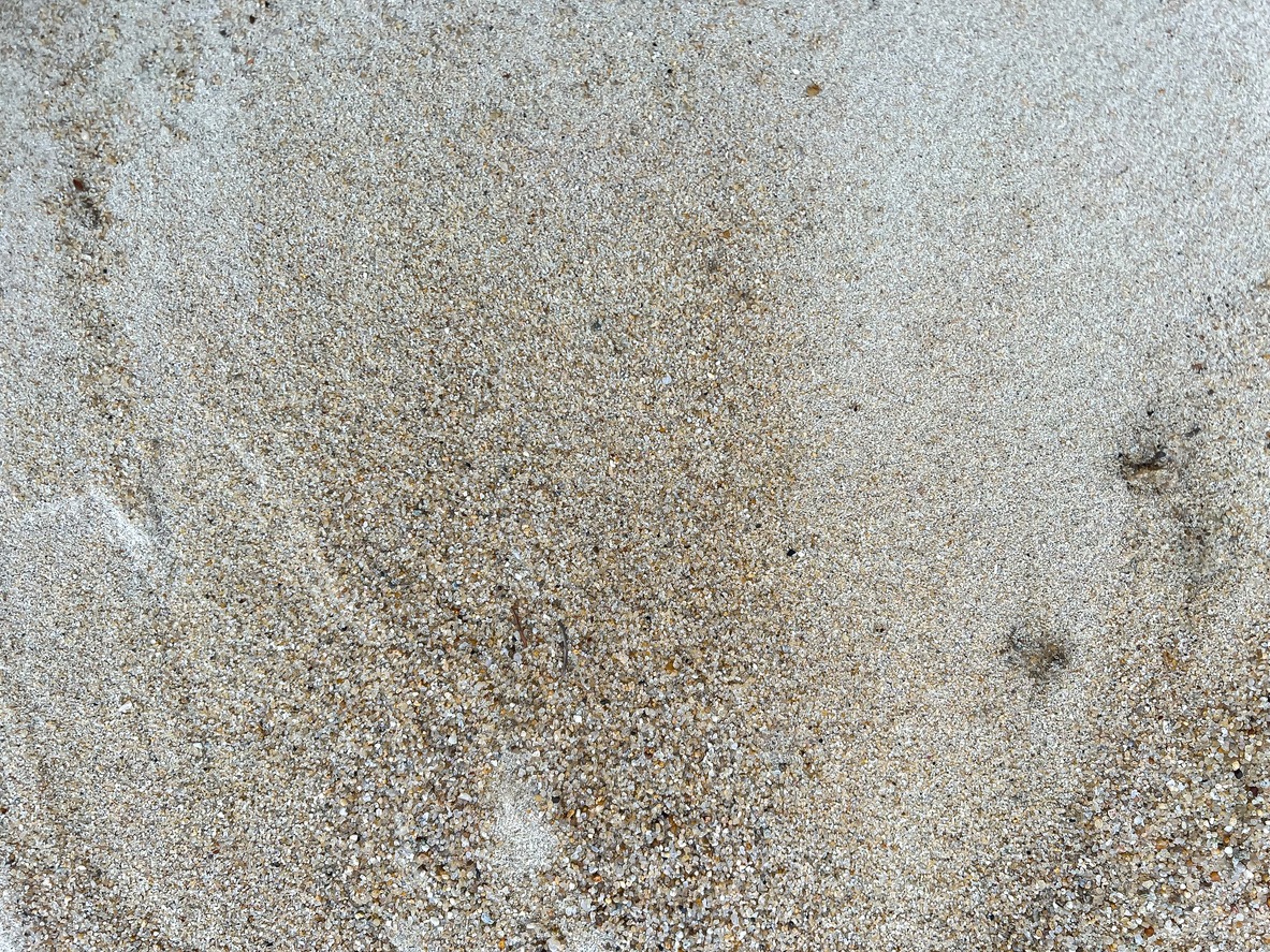 A close-up of sand with fine grains and small pebbles, creating a textured surface. No landmarks or buildings are visible.