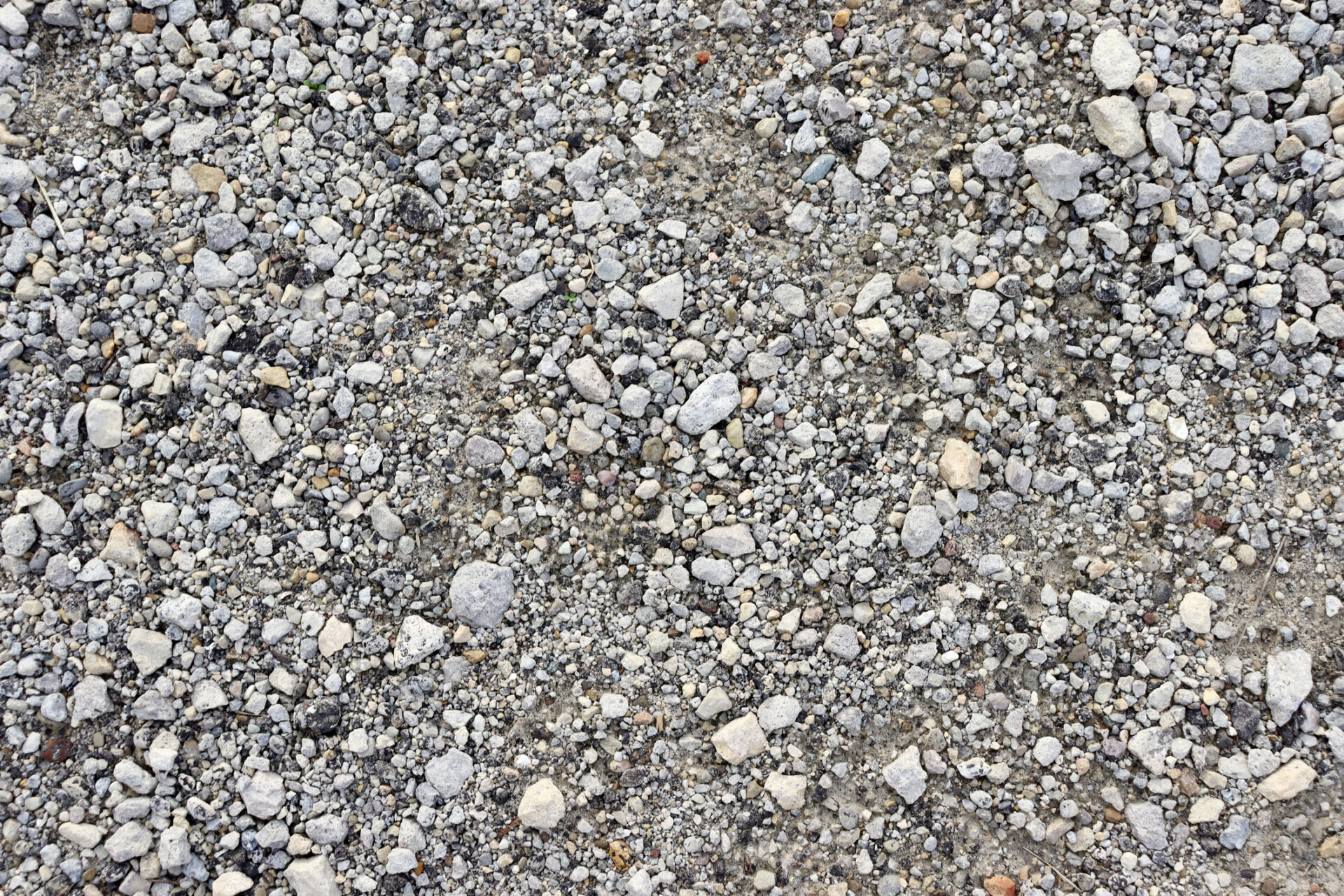 Close-up view of a gravel surface, showcasing a variety of small and medium-sized stones in shades of gray, spread evenly across the ground.